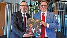 Landrat Sven Hinterseh (links) überreicht Regierungspräsiden Carsten Gabbert einen prächtigen Bildband mit Motiven aus dem Landkreis.