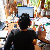 Eine Frau arbeitet mit Hörschutz im Homeoffice. Laut kann es daheim werden, wenn Kinder auch zuhause sind – doch die Corona-Gefahr ...