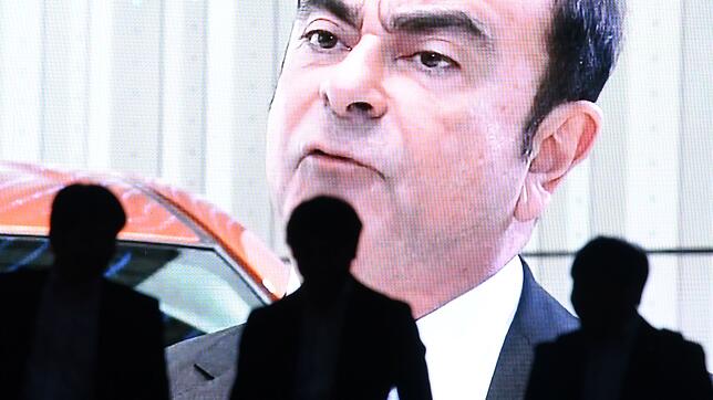 Passanten stehen in Tokio vor einem großen öffentlichen LED-Bildschirm und verfolgen einen Nachrichtenbericht über den Skandal um Carlos ...