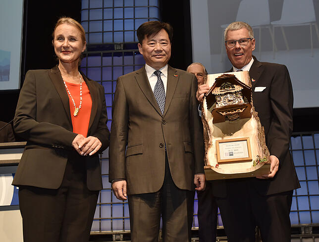 Thomas Weisser (rechts) übergibt mit IHK-Präsidentin Birgit Hakenjos-Boyd dem chinesischen Botschafter Wu Ken eine Kuckucksuhr.