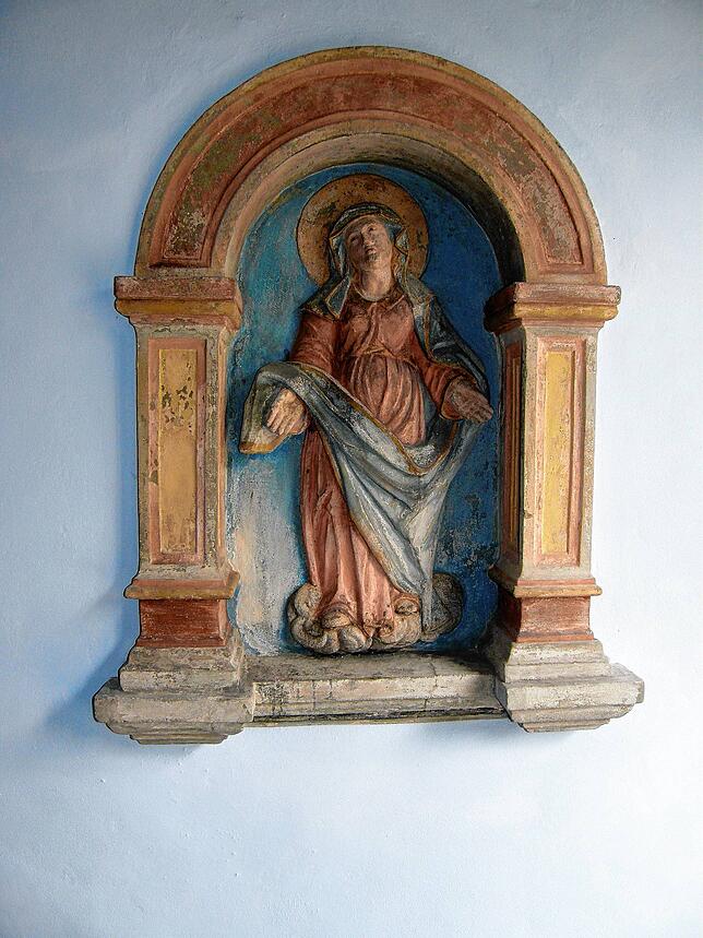 In einer Wandnische ist die Muttergottes Maria dargestellt. Es ist möglich, dass gegenüber früher das Kruzifix war, das heute in der ...