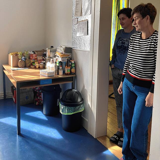 Maria und Olha Mekh blicken in die Küche. Dort steht ein Tisch mit Lebensmittel, die gespendet wurden.