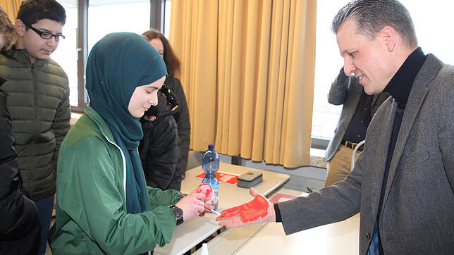 Realschülerin Meryem Erdem bemalt die Hand des Bundestagsabgeordneten Thorsten Frei für den Abdruck zum Red Hand Day.