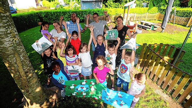 Ein Teil der Kinder der orangenen und blauen Gruppe, die das Plakat mit den Störchen mit Handabdrücken gestaltet haben, freuen sich ...