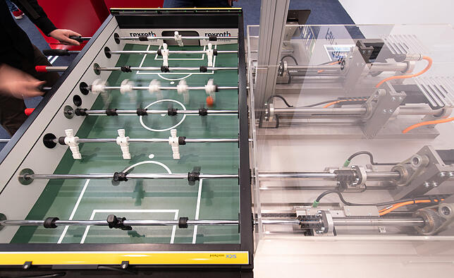 Ein Roboter des Herstellers Bosch Rexroth AG spielt Tischfußball mit einem Messebesucher.