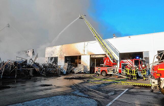 Einsatzkräfte der Feuerwehr stehen während eines Großbrandes auf dem Gelände eines Reifengroßhändlers und löschen das Feuer.