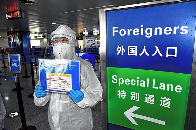 Ein Mitarbeiter in Schutzanzug erinnert mit einem Schild Reisende aus dem Ausland am chinesischen Qingdao Liuting International ...