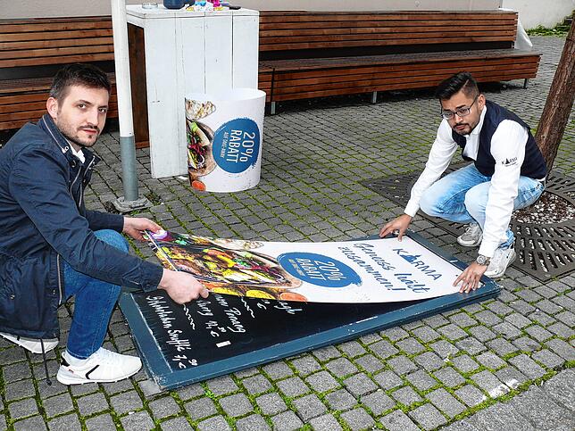 Arianit Saiti und Vijay Kumar, Mitarbeiter des Restaurants Karma in der Unnenstadt, ziehen die Plakate für den neuen Catrering-Service auf.
