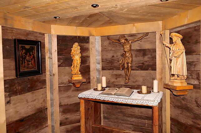 Im Inneren der Kapelle geben alte und neue Baumaterialen ein harmonische Bild. Über dem Altar hängen handgeschnitzte Holzfiguren.