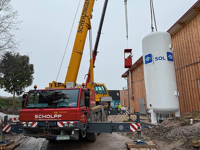 Mit einem Tragekorb wird einer der Arbeiter zum Tank hochgehoben, um dort die schweren Trageseile abmontieren zu können.