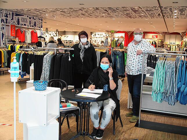 Andrea Keller sitzt im Modehaus Heikorn am Eingang und registriert alle Besucher. Hinter ihr freuen sich Bettina und Thomas Kornmayer ...