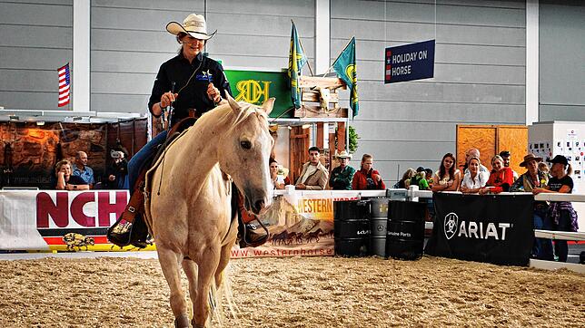 Eine Reiterin zeigt bei der Americana, wie Horsemanship funktioniert, und lenkt ihr Pferd souverän im Westernsattel ganz ohne Trense.