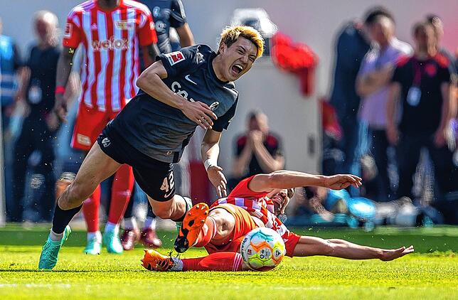 Berlins Rani Khedira (r) foult Ritsu Doan von SC Freiburg und sieht im Anschluss dafür die Gelbe Karte.