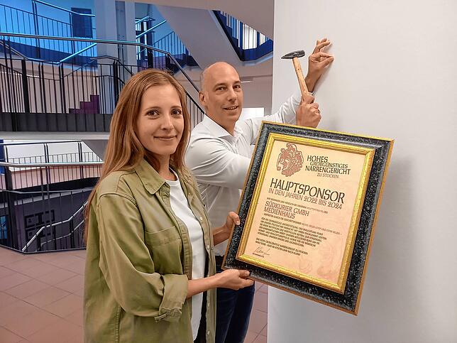 Tobias Gräser und Franziska Schicht hängen die Urkunde im SÜDKURIER Medienhaus in Konstanz auf.