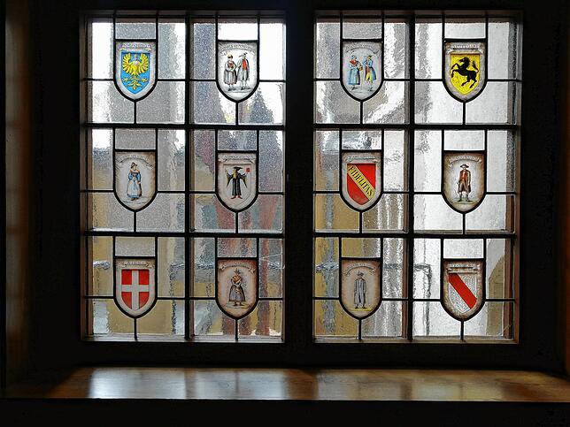 Wappen von Wien bis Straßburg und Figuren in Schwarzwälder und Steiermärker Trachten zieren die Buntglasfenster in den Schwarzwaldstuben.