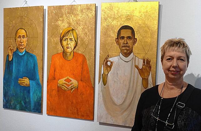 Olga David neben ihren Politikerporträts &bdquo;Barack &ndash; Angela &ndash; Vladimir&ldquo;.