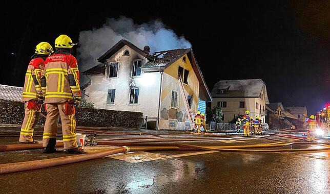 Feuerwehrleute schauen auf die Brandruine.