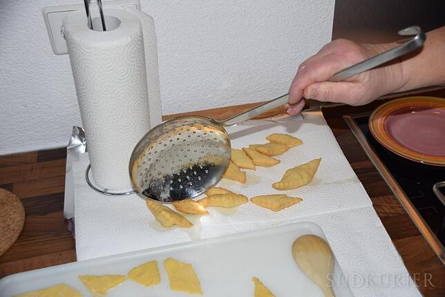 Hole die fertig ausgebackenen Küchle mit einer Schöpfkelle aus dem Topf und lasse sie auf dem Küchenpapier abtropfen. Danach mit einem ...