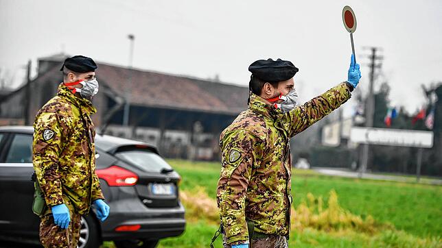 Ein Soldat mit Atemschutzmaske hält an einer Straßensperre vor der roten Zone von Turano Lodigiano eine Winkerkelle in die Höhe.