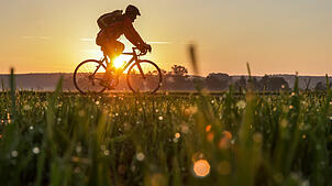 Ein Radfahrer ist am 10. August 2025 am Morgen im Sonnenaufgang bei Riedlingen unterwegs. Dem Südwesten stehen heiße Tage bevor.