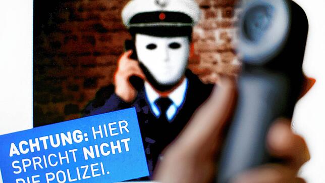 Ein Telefonhörer ist vor einem Plakat der Polizei mit der Aufschrift &bdquo;Achtung: Hier spricht NICHT die Polizei&ldquo; zu sehen. ...