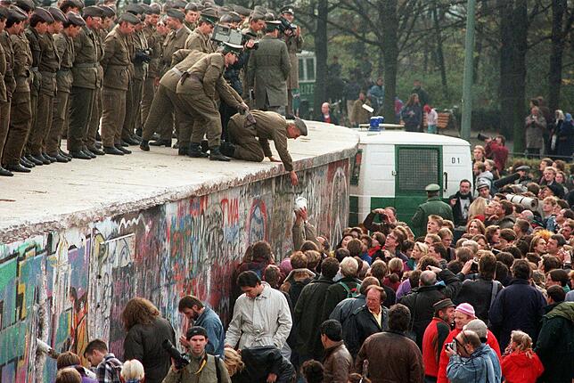 11. November 1989: DDR-Grenzposten stehen auf der Mauer vor dem Brandenburger Tor und sprechen zu DDR-Bürgern, die durch die Stadt strömen.