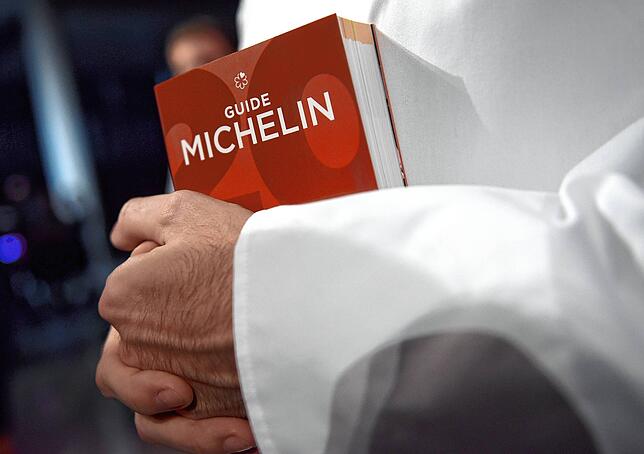 Ein Koch hält den Restaurantführer Guide Michelin in der Hand. Spitzengastronomen und Feinschmecker blicken mit Spannung auf die ...