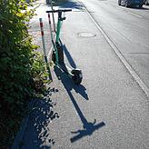 Ein E-Roller blockiert Teil des Gehweges.