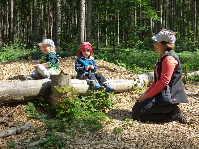 Sophia und Marla mit Erzieherin Franziska Nusser haben es sich auf einem Baumstamm bequem gemacht.
