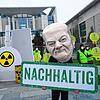 Ein als Bundeskanzler Scholz verkleideter Aktivist steht mit einem Transparent mit der Aufschrift &bdquo;Nachhaltig&ldquo; vor einem ...