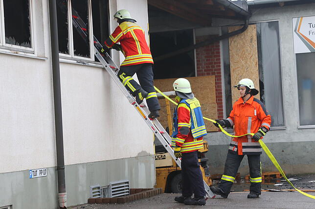 Ein Feuerwehrmann steigt für die Bekämpfung von Glutnestern auf eine Anlegeleiter an der ausgebrannten Halle.
