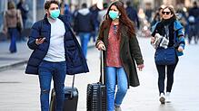Touristen tragen in Mailand Mundschutz und rollen ihre Gepäck. Angesichts der raschen Ausbreitung des neuen Coronavirus in Italien macht ...