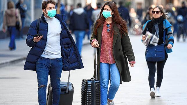 Touristen tragen in Mailand Mundschutz und rollen ihre Gepäck. Angesichts der raschen Ausbreitung des neuen Coronavirus in Italien macht ...