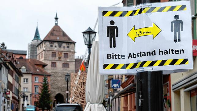 Ein Hinweisschild mit der Aufschrift &bdquo;Bitte Abstand halten&ldquo; hängt an einer Straßenlaterne in der Fußgängerzone von Rottweil. ...