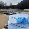 Das Foto zeigt den Bauplan für die Freibadsanierung vor dem leeren Schwimmerbecken. Das blaue Männchen auf dem Beckenboden &ndash; ...