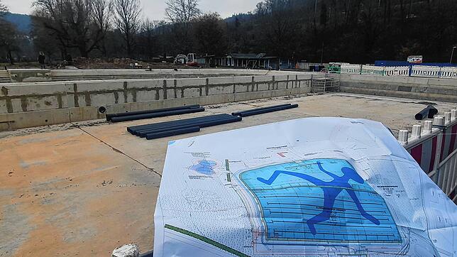 Das Foto zeigt den Bauplan für die Freibadsanierung vor dem leeren Schwimmerbecken. Das blaue Männchen auf dem Beckenboden &ndash; ...