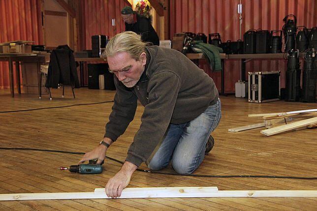 Götz Knieß schraubt das Holzgestänge für die Bühnenvorhänge zusammen.