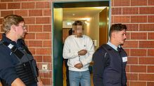 Einer der Angeklagten wird von Wachtmeistern in den Verhandlungssaal geführt.