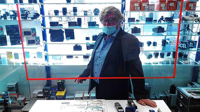 Doppelte Sicherung mit Plexiglasscheibe und Maske: Seniorchef Ralf Dockhorn steht an einer Ladentheke im Waldshuter Fotofachgeschäft ...