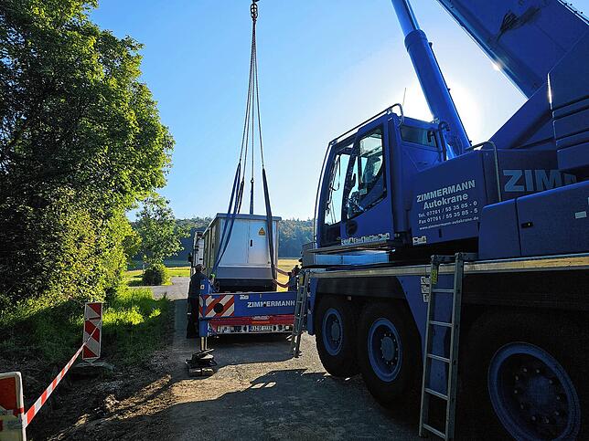 Der Fahrer eines Autokrans bewegt die Trafostationen vom Lastwagen.