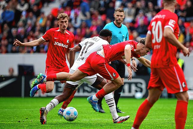 Freiburgs Noah Weißhaupt (2.v.r.) kommt im Duell mit St. Paulis Oladapo Afolayan (2.v.l.) zu Fall.