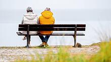 Zwei ältere Menschen sitzen bei trübem Wetter auf einer Bank. Die Aussichten für das Alter sind in anderen Ländern besser.