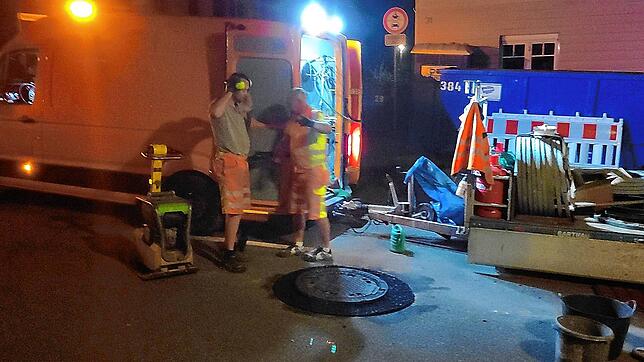 Mit der Rüttelplatte befestigen die Arbeiter den frischen Asphalt um den ausgetauschten Gullideckel herum.