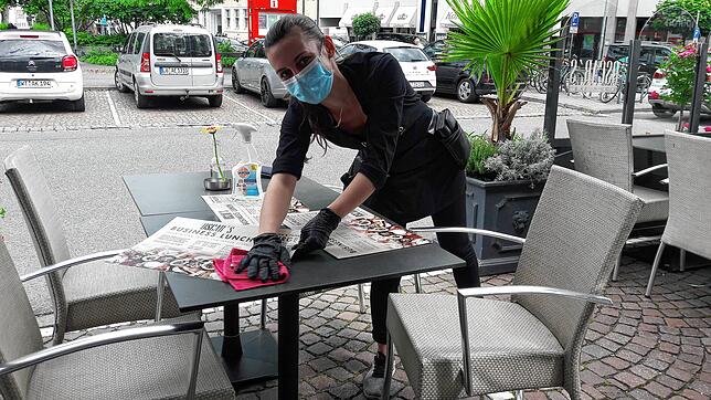 Servicemitarbeiterin Désirée Weiß, die Mundschutz und Handschuhe trägt, desinfiziert die Tische auf der Gartenterrasse des Oscar‘s ...