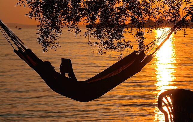 Bayern, Lindau: Eine Frau liest in einer Hängematte am Badestrand eines Campingplatzes ein Buch.