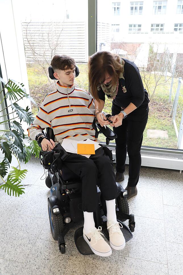 Manuela Pagels befestigt die Klammer an Jannis‘ Hand. Damit kann er einen Stift führen.