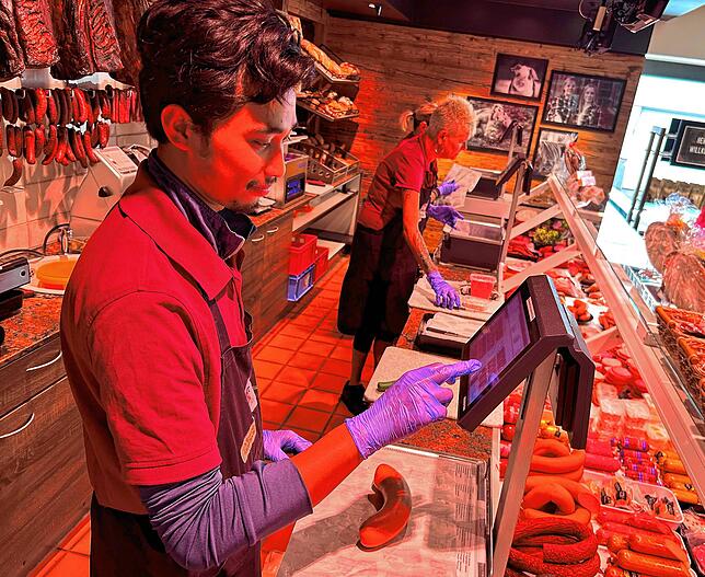 Agil Prastyo beim Bedienen hinter der Wursttheke. Im täglichen Kontakt mit den Kunden übt er seine Sprachkenntnisse. Die Kassencodes für ...