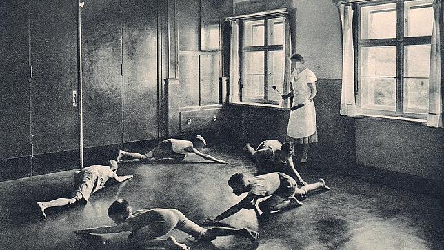 Fünf Buben kriechen nach Trommelschlag einer Betreuerin über den Boden in einem Kinderkurheim. Heute sind viele ehemalige Kurkinder an ...
