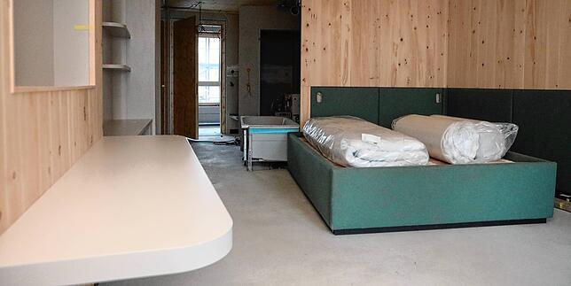 Die Wände sind aus Zirbenholz gefertigt, auf den Boden kommt Eiche. Das Bett und die Wand dahinter sind mit grünem Lodenstoff verkleidet.