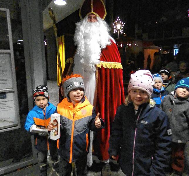 Der Nikolaus verteilt an kleine Weihnachtsmarktbesucher schokoladige Weihnachtsmänner.